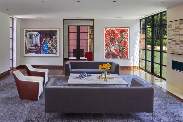 The living room features floor-to-ceiling black-framed windows and colorful wall art on white walls.