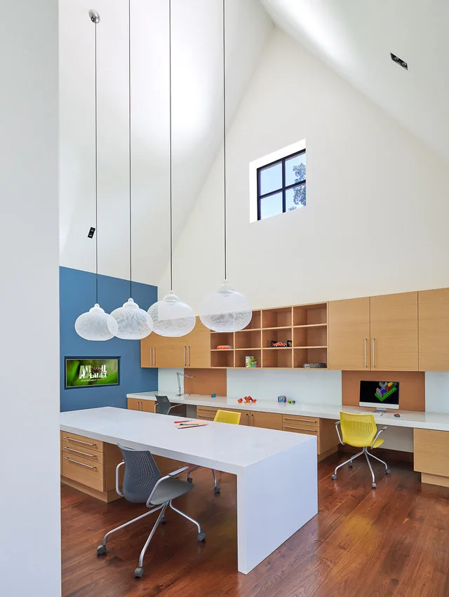 This home office features vaulted ceilings, custom wood cabinetry, a large white desk, and globe pendant lighting.