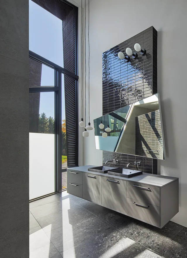 PTR HOUSE bathroom features a floating double vanity with two rectangular sinks and an angled mirror on a tall black tile wall.