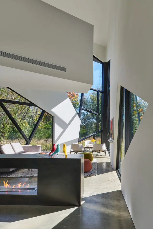 Living room of PTR HOUSE features angular black window frames and a linear fireplace within a dark partition wall.