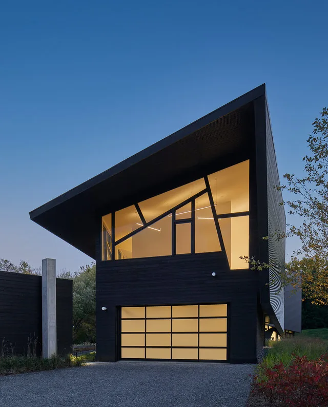 PTR HOUSE by Robert Gurney Architects features an angular roof and geometric window design with dark ribbed siding.