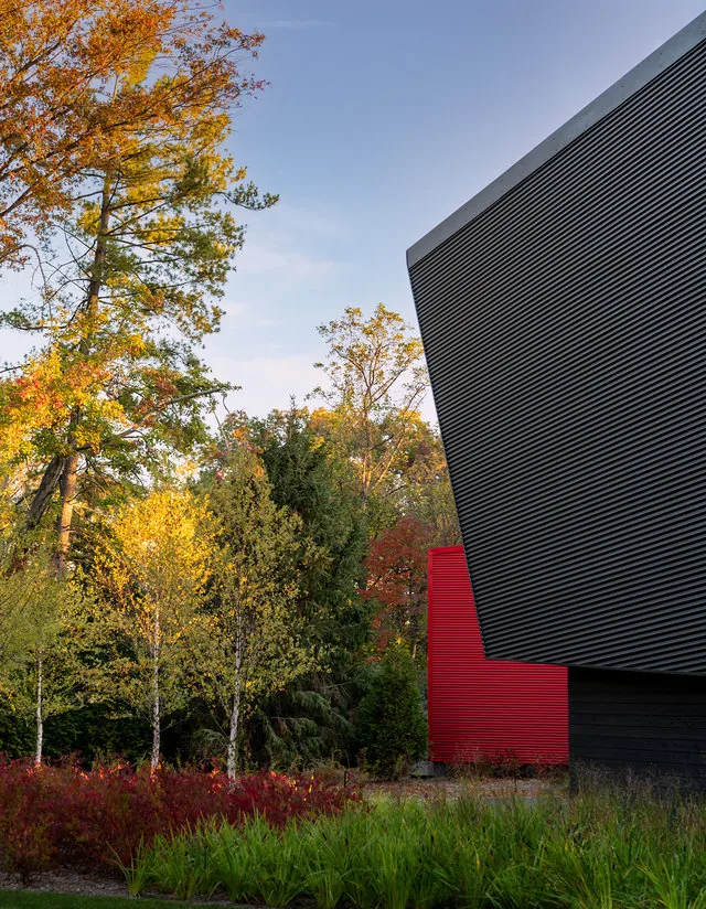 Black and red angular exterior walls of PTR HOUSE contrast with surrounding colorful autumn trees.