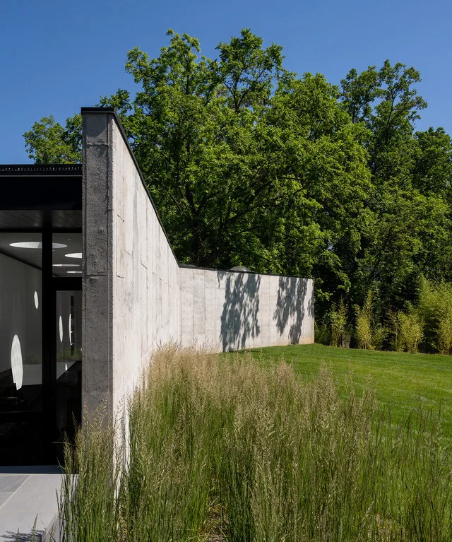 PTR House features a textured concrete wall with circular window apertures casting shadows inside, surrounded by natural landscaping.