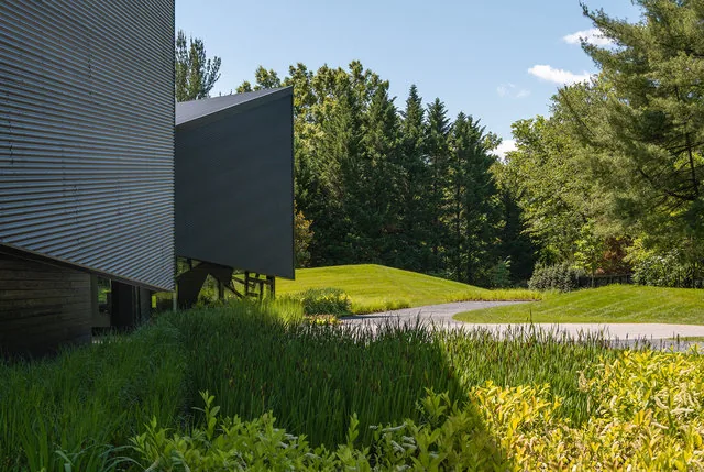 PTR HOUSE features angular design with dark stained wood siding and a sloped metal roof edge amidst autumn landscaping.