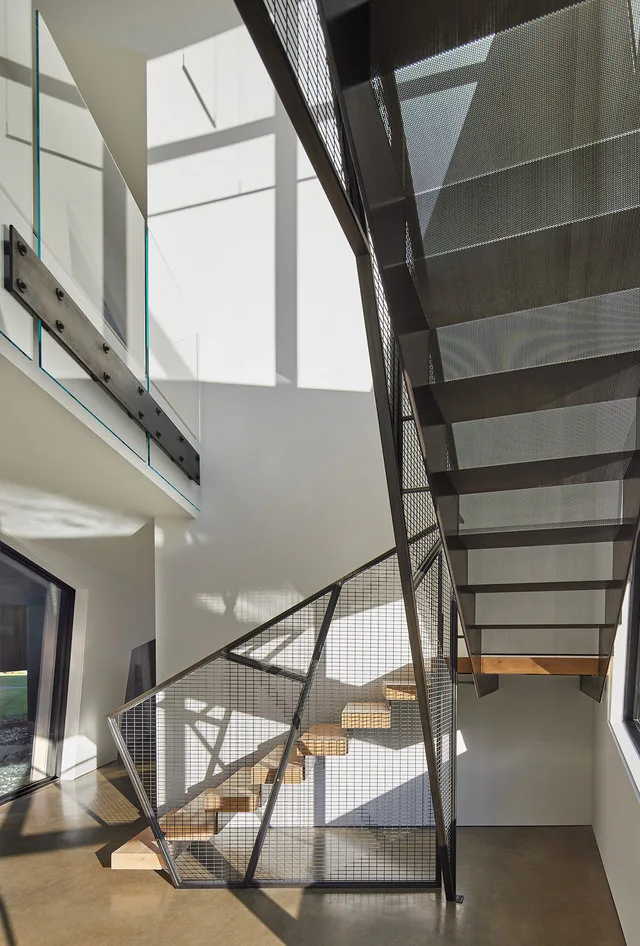 Marble-floored stairwell with metal mesh railing and wooden steps illuminated by natural light.