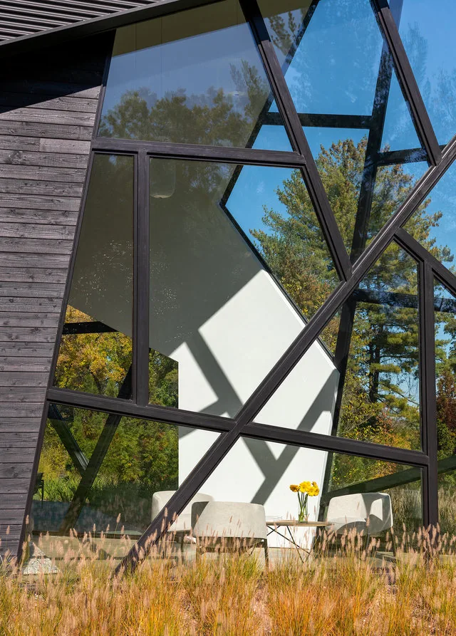 PTR HOUSE features angular black framed windows and dark wood siding, with a glimpse of the interior seating area.