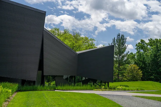 PTR HOUSE by Robert Gurney Architects features angular walls with dark ribbed siding and triangular long narrow windows framed by an angular roof.
