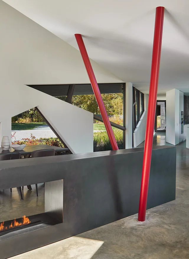 Modern interior space in the PTR HOUSE features red angled columns, triangular windows, and a linear fireplace within a black partition.