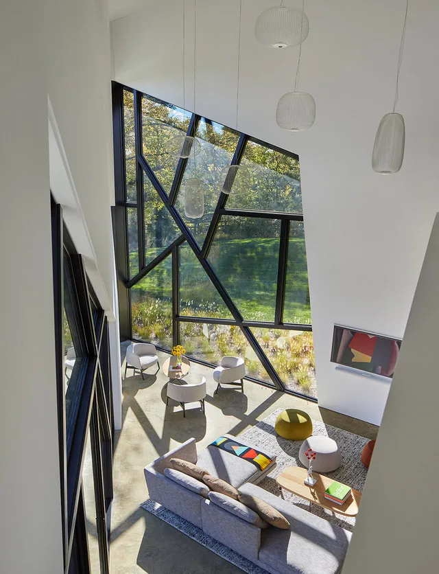 Living room with large triangular and angular windows casting geometric shadows and outfitted with contemporary furniture.