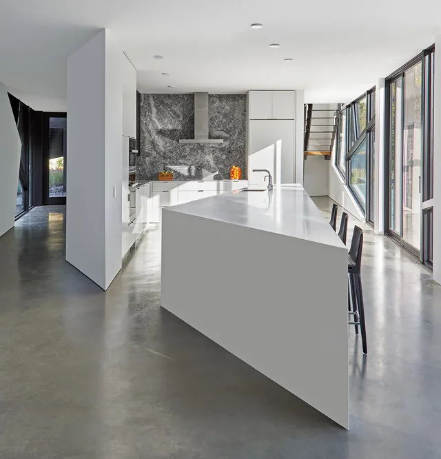 PTR HOUSE kitchen by Robert Gurney Architects features an angular white island and polished concrete floor with angled windows providing natural light.