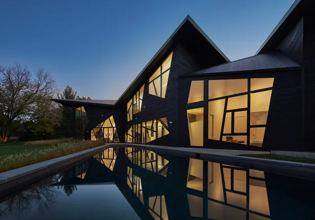 The PTR HOUSE features asymmetrical windows and vertical siding, reflecting in a rectangular pool at dusk.
