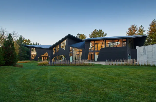PTR HOUSE by Robert Gurney Architects features dark stained wood siding and black window frames in a modern angular design.