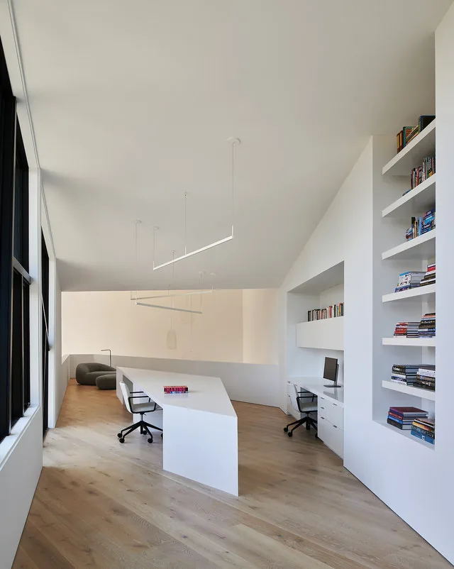 PTR HOUSE study area with white built-in shelving, an angular desk, and natural wood floors.