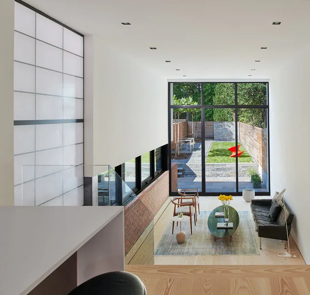 Modern living room with large black window frames and a view to a fenced backyard featuring a red sculpture in RENOVATION 1662.