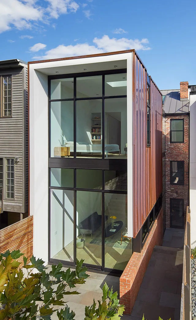 A contemporary two-story home with floor-to-ceiling black window frames and a combination of brick, white, and metal exterior.