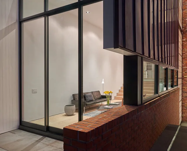 Exterior view of RENOVATION 1662 showing black-framed floor-to-ceiling glazing and brick wall.
