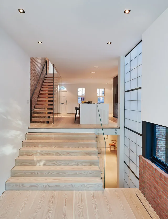 Modern interior with light wood floating stairs, glass railing, and a brick accent wall near the shoji-style window.