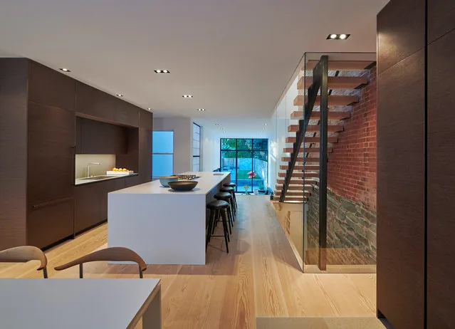Interior view of modern kitchen featuring a white island, dark wood cabinetry, and floating stairs adjacent to brick and stone wall.
