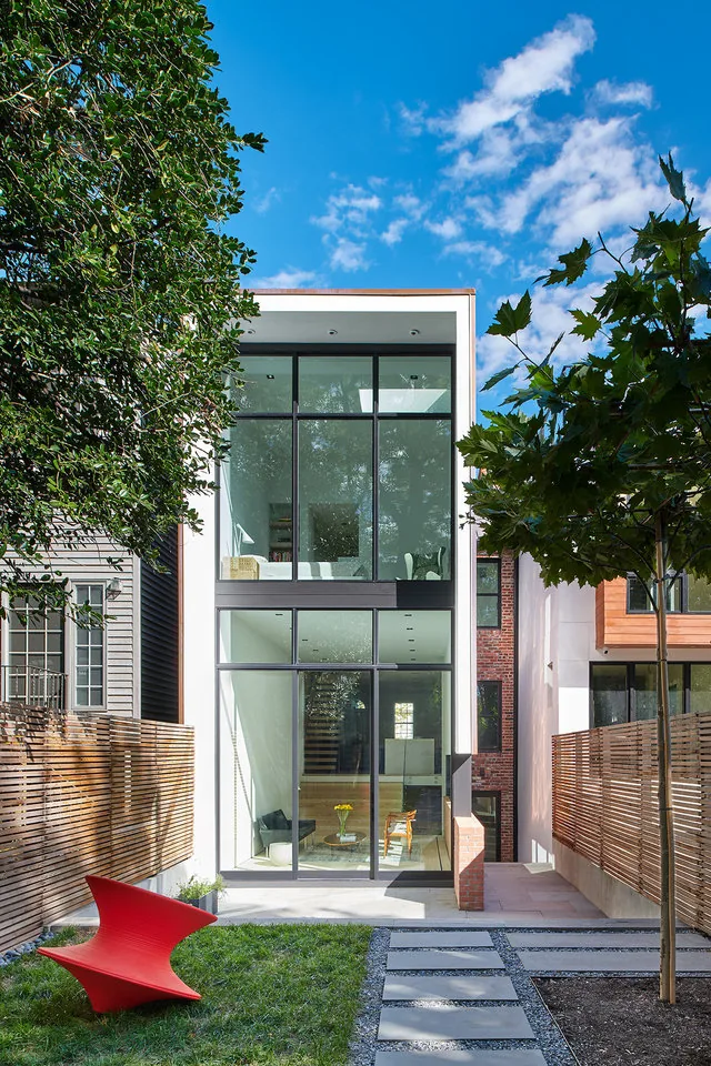 Modern two-story home featuring floor-to-ceiling black-framed windows and a contemporary backyard design with pathway.