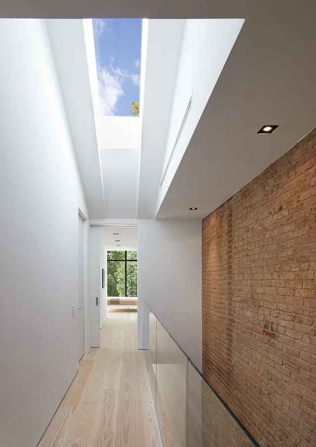 Hallway features skylights and an exposed brick accent wall with light wood flooring.