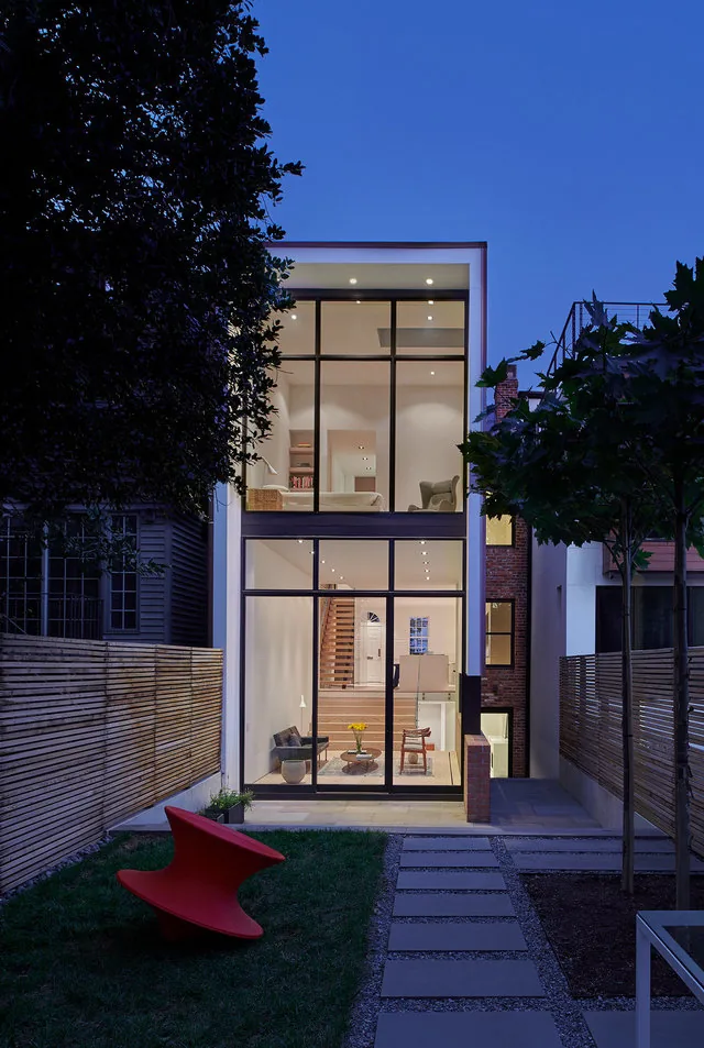 Exterior rear view of RENOVATION 1662 showing large glazing and a backyard patio at dusk.