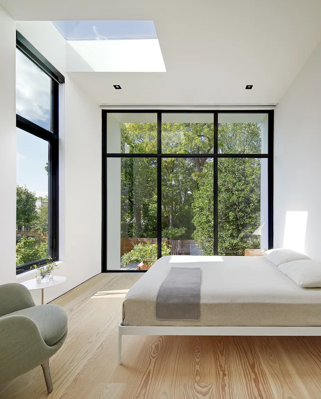 The bedroom features floor-to-ceiling black metal-framed windows and a skylight providing ample natural light.