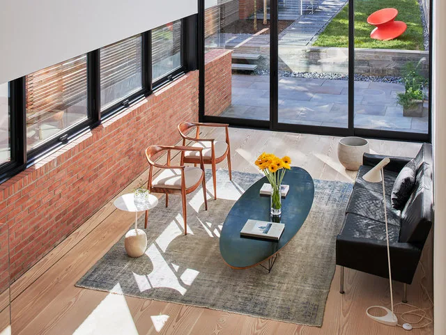 A living room featuring black metal window frames, exposed brick walls, and light wood floors in RENOVATION 1662.