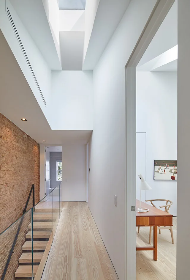 Renovated hallway featuring exposed brick wall, glass stair railing, light wood floor, and natural light from skylight.
