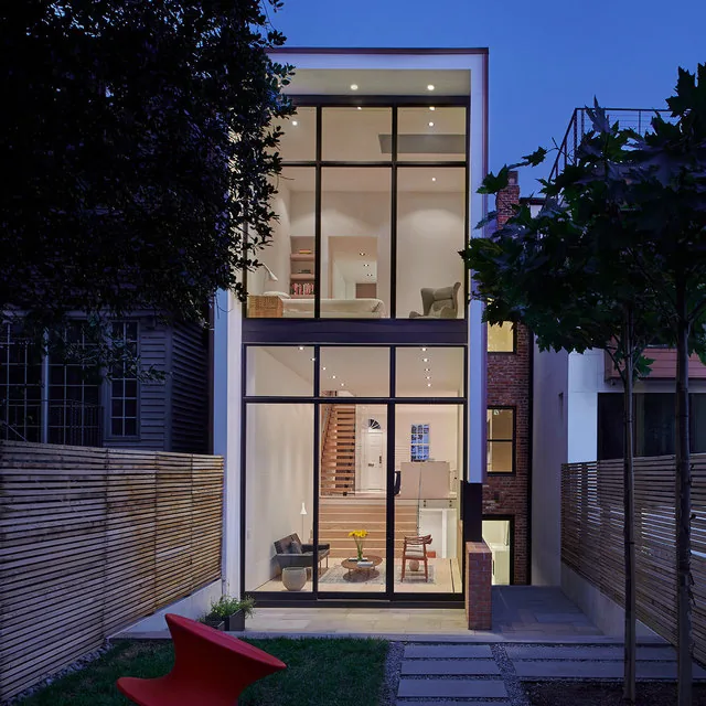 RENOVATION 1662 features a modern two-story home with large windows and mixed material exterior, viewed from the green backyard with stepping stone path.