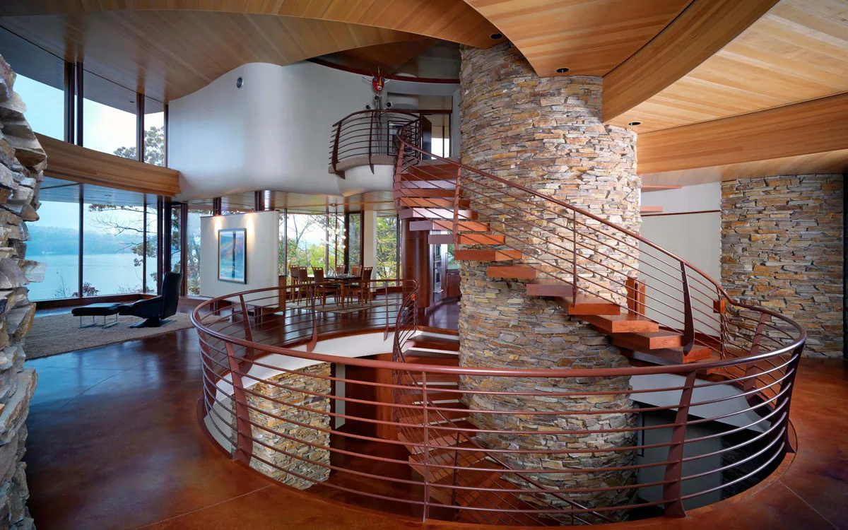 Curved metal railing staircase around stone columns with wood ceiling and lake views.