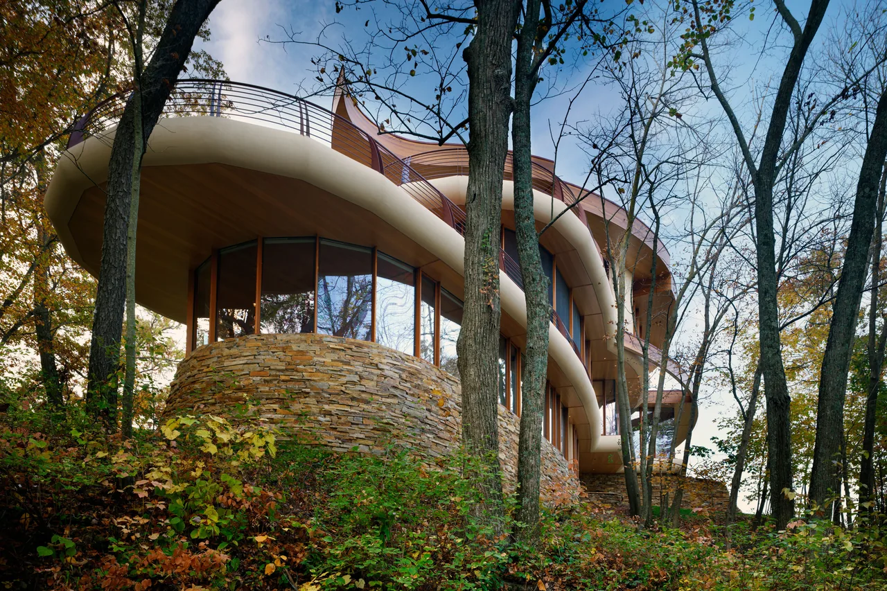 Chenequa Residence features a curved exterior wall with stone veneer and large glass windows under a wood soffit with curved railing above.