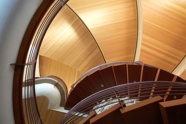 Curved wooden staircase with a metal railing and wood-paneled ceiling in the Chenequa Residence by Robert Harvey Oshatz Architect.