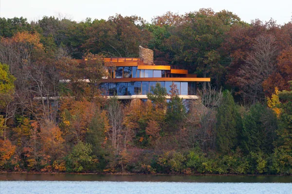Chenequa Residence by Robert Harvey Oshatz Architect features extensive glazing and a stone chimney on a wooded hillside.