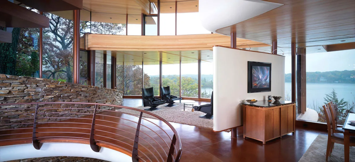 Interior view of a living space featuring stone accents, curved wood railing, and large windows with lake views.