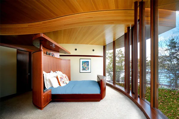 Chenequa Residence bedroom features a curved wood bed and ceiling with floor-to-ceiling windows looking out to the lake.