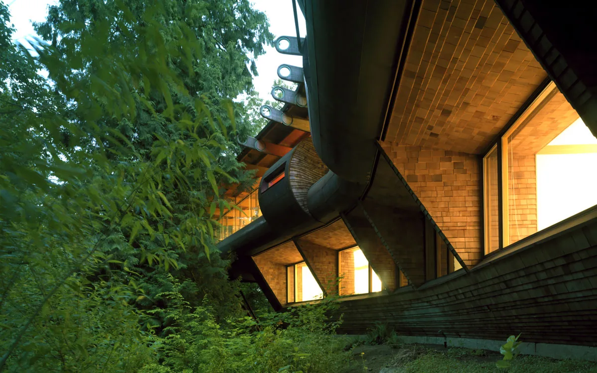 The Wilkinson Residence features a curved wood-shingled exterior wall and roof set in a forest environment.