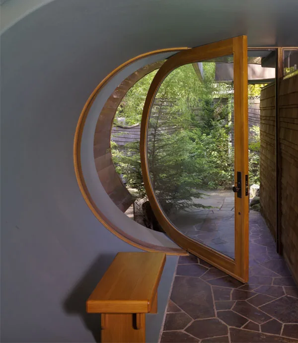Curved circular door with wood frame opens to an outdoor garden area with stone flooring at Wilkinson Residence.