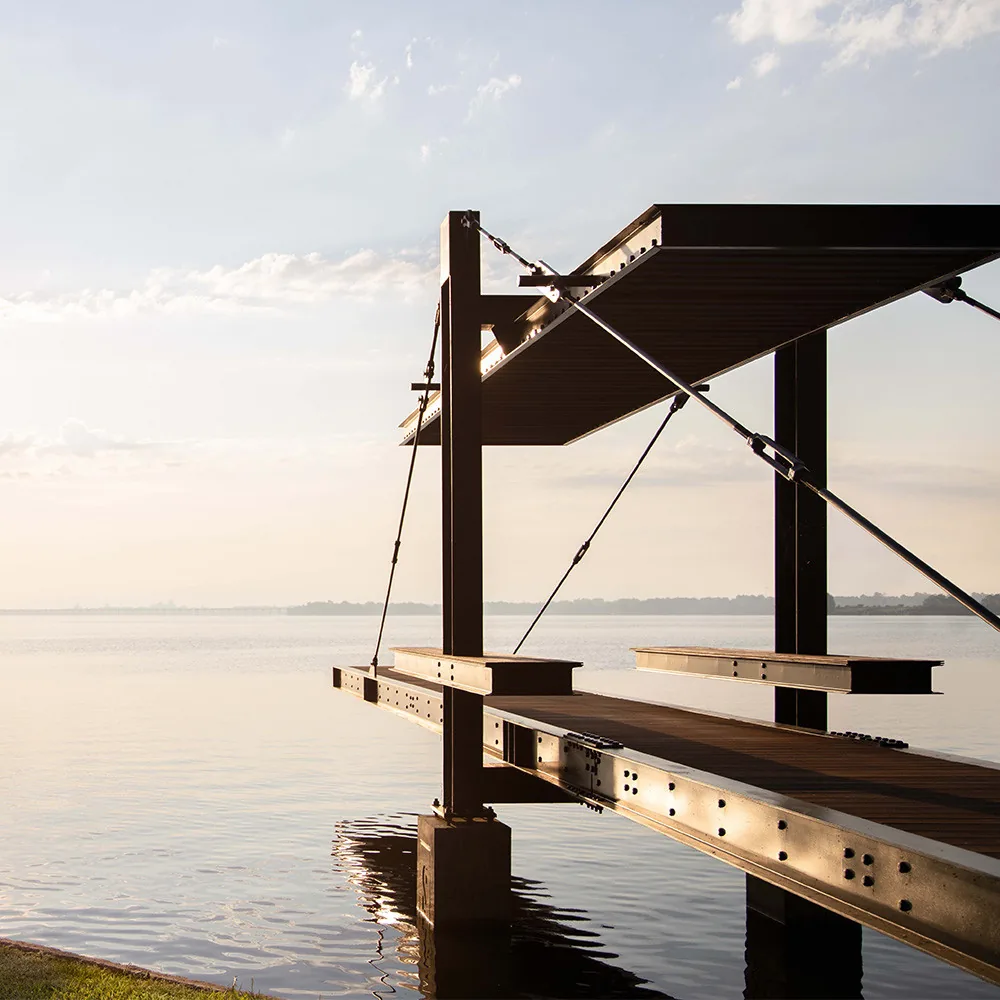 Modern dock structure with steel beams and wood decking over water at sunrise or sunset.