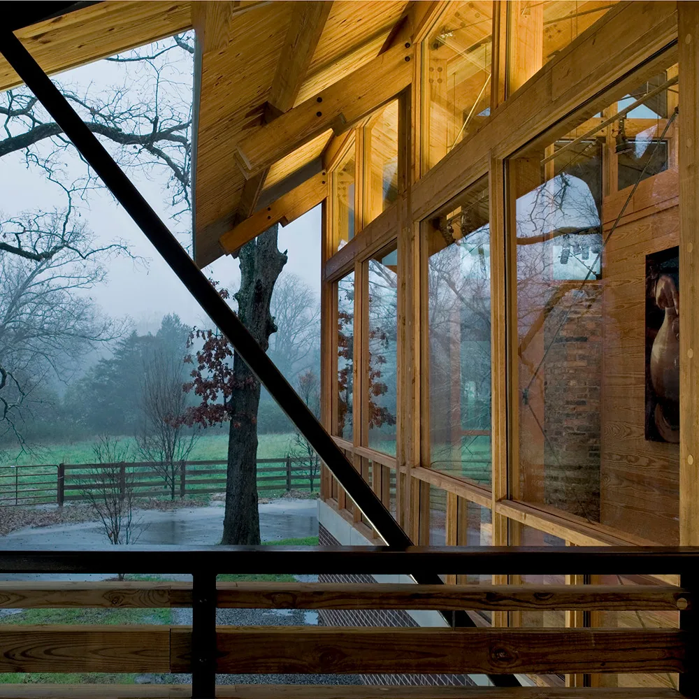Wood-clad exterior with floor-to-ceiling vertical windows and a diagonal metal brace on a rainy day.