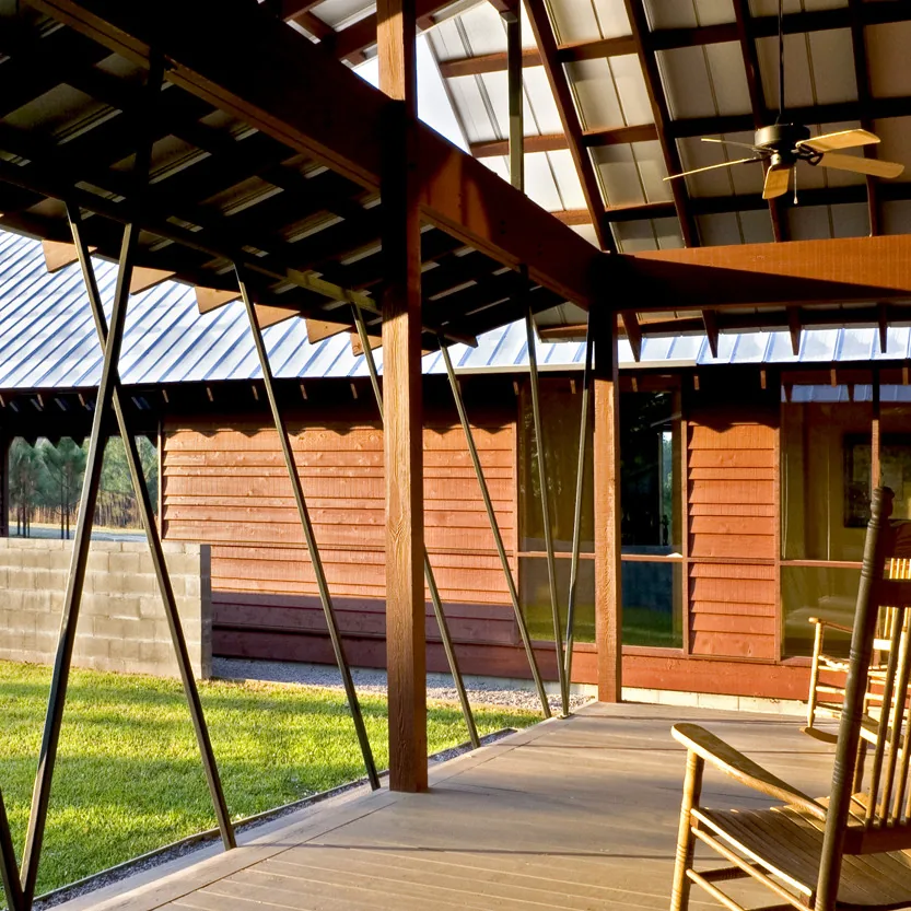 The covered porch features a metal roof with exposed wooden beams and braces, and two wooden rocking chairs on a concrete floor.