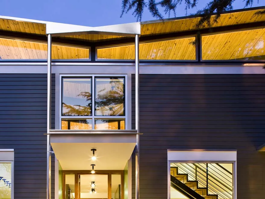 Modern exterior of a house featuring dark wood siding and a butterfly roof with prominent clerestory windows.