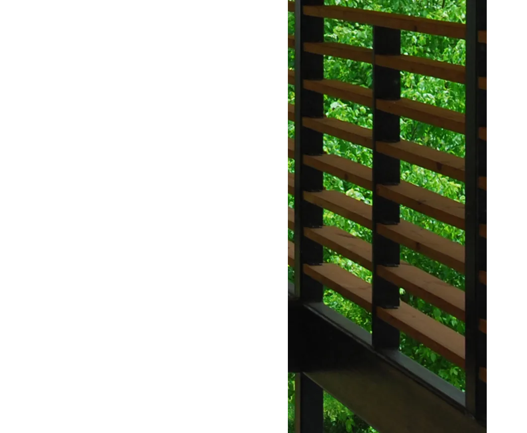 Detail of a horizontal wooden railing with black metal framing against a backdrop of green foliage.