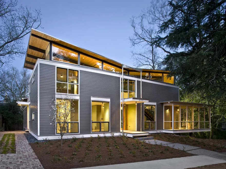 Modern two-story house with wood siding, clerestory windows, and a covered screened porch taken at dusk.