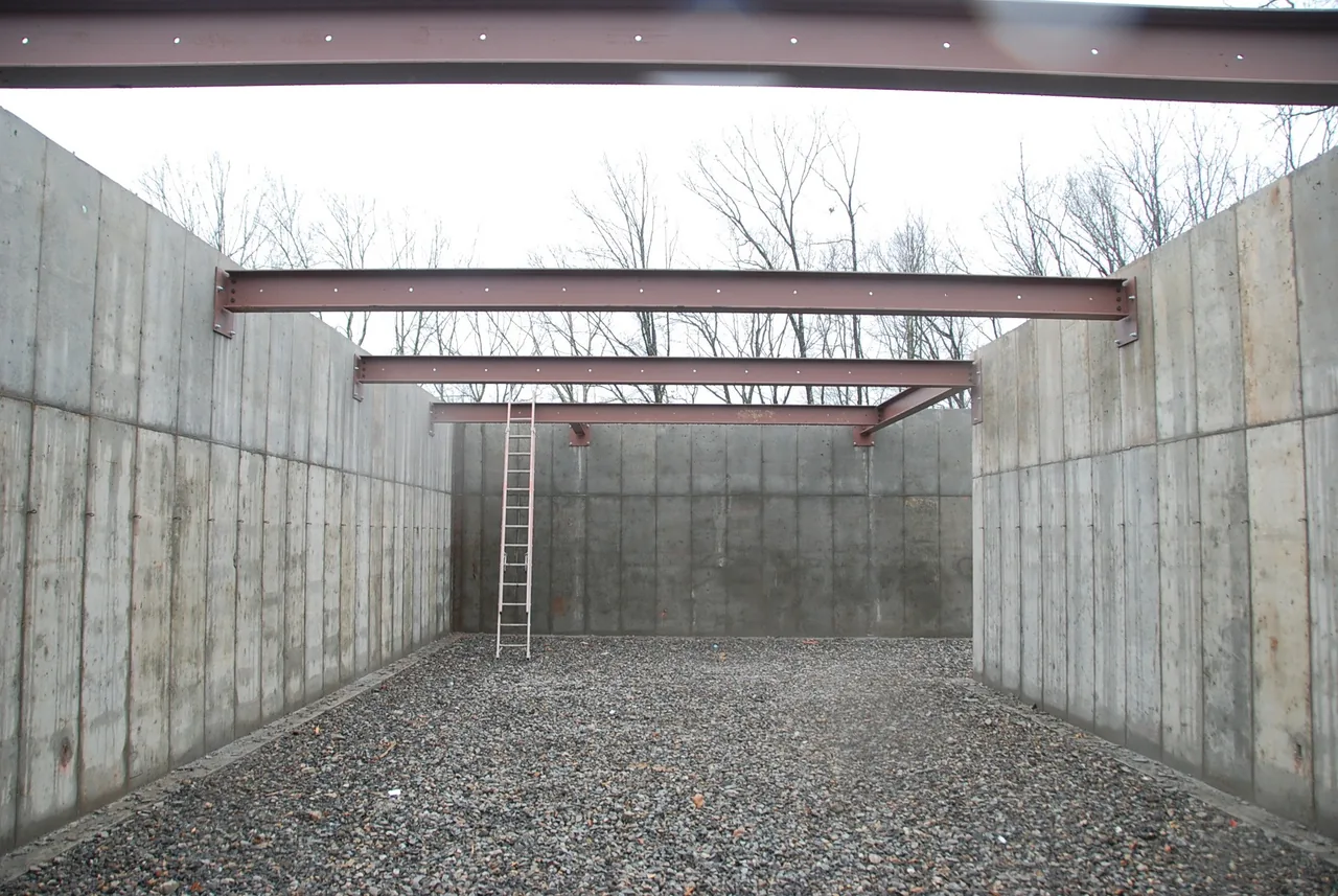 Concrete walls with steel support beams above an unfinished interior space under construction.