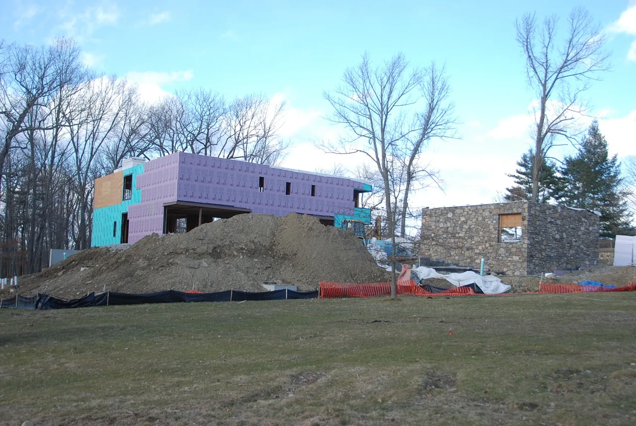 Construction site of House 432 showing two buildings in progress with insulation and stone cladding.