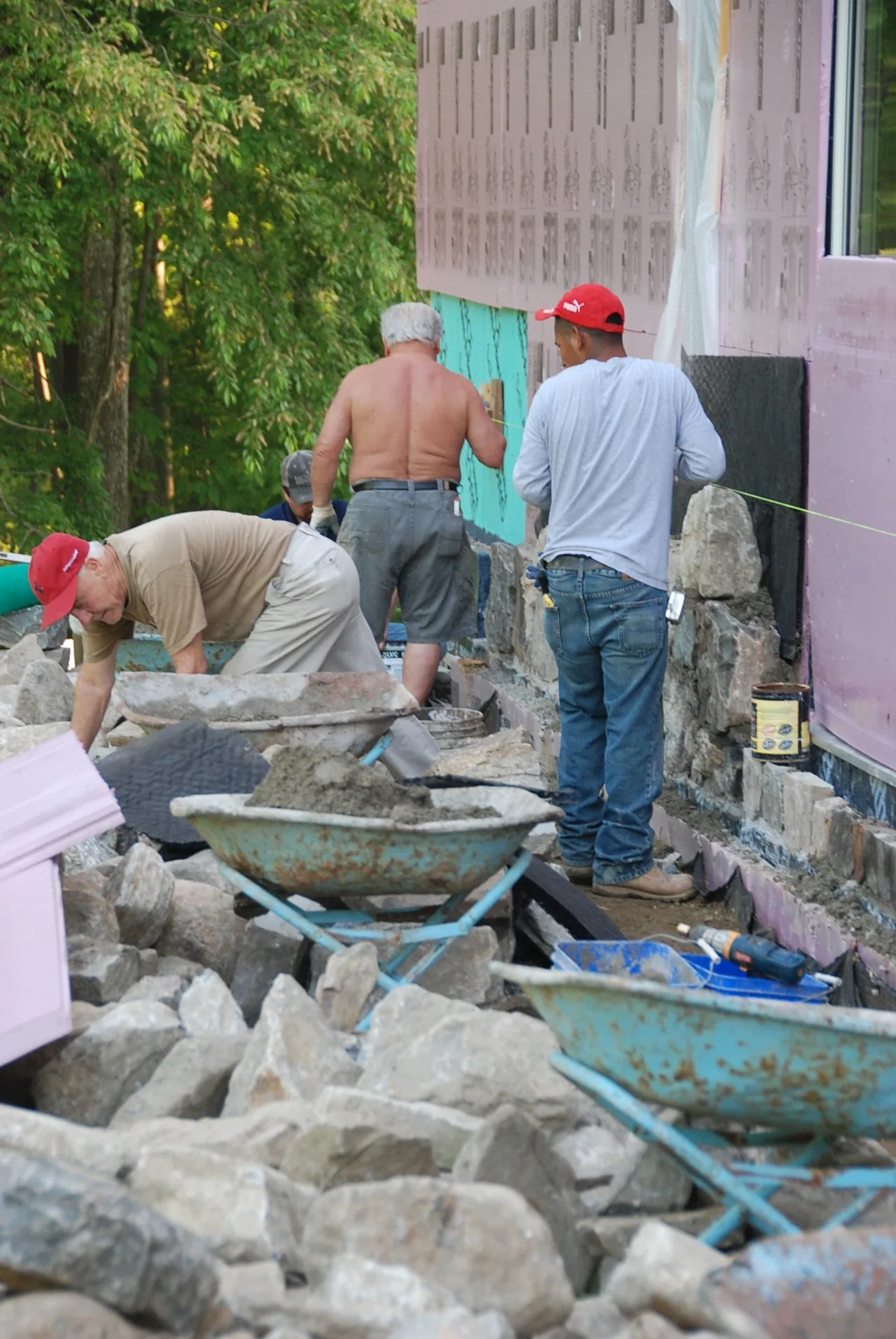 Workers are applying stone exterior cladding on a partially insulated home under construction.