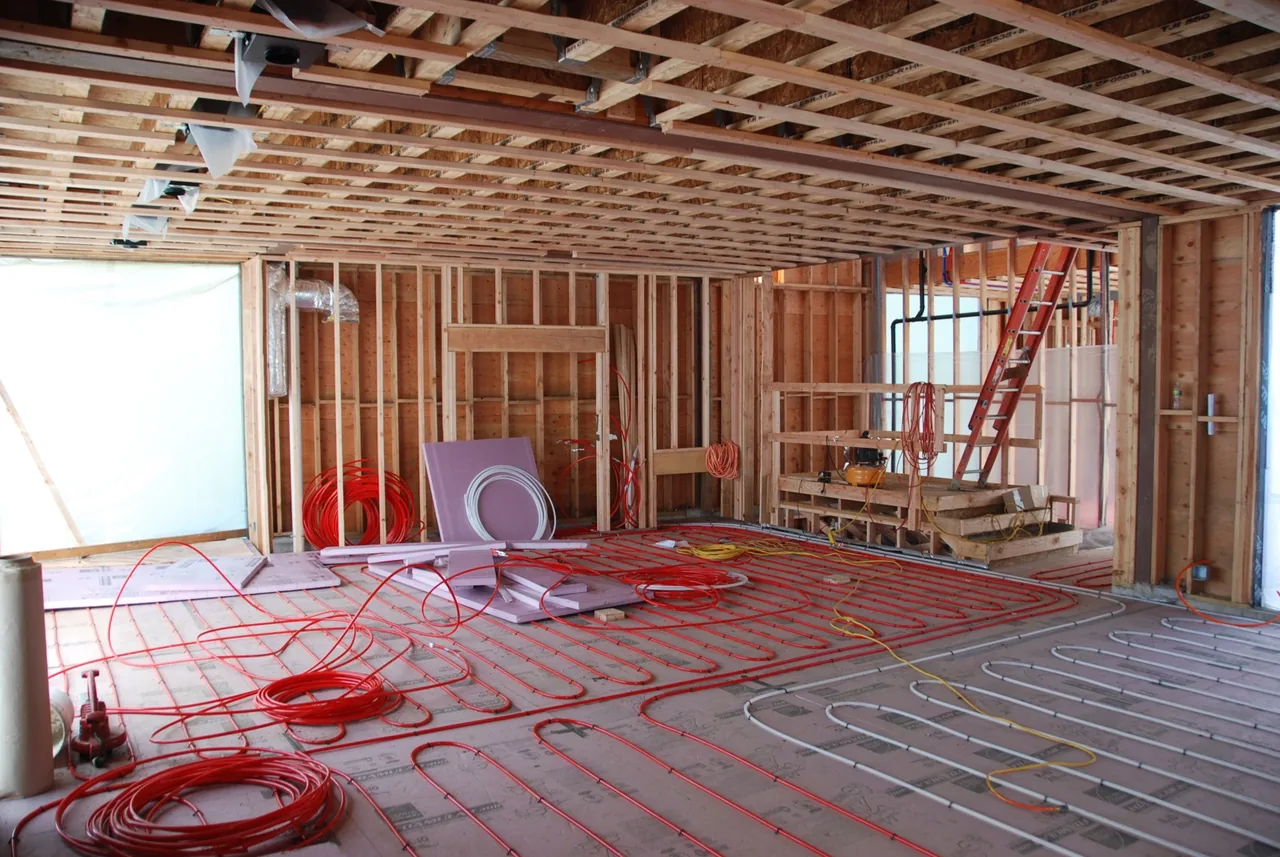 Room under construction with visible wood framing and radiant floor heating tubes before flooring installation.