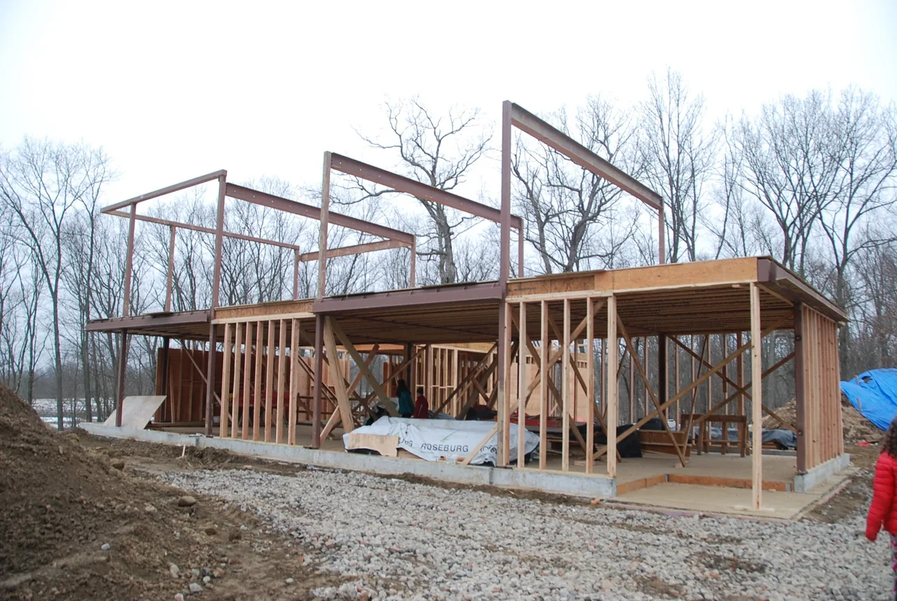 House 432 wood frame and steel skeleton structure in early construction phase with concrete foundation visible.