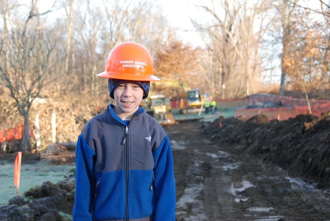Construction site of House 432 with a young person wearing a Robert Siegel Architects helmet in the foreground.