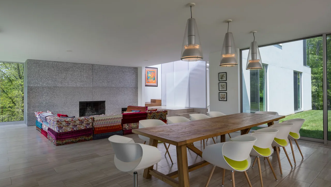 Open living and dining room with a wood dining table and colorful sectional sofa near a stone fireplace wall in House 432.